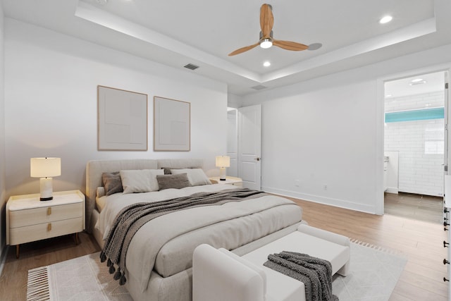 bedroom with hardwood / wood-style floors, a tray ceiling, ceiling fan, and ensuite bathroom