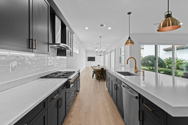 kitchen with sink, light stone counters, decorative light fixtures, a large island with sink, and appliances with stainless steel finishes