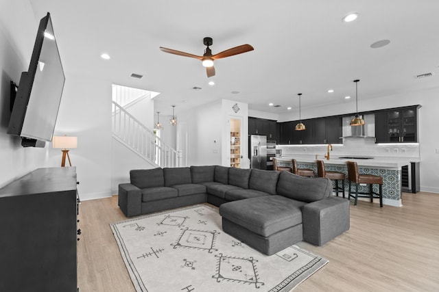 living room with ceiling fan with notable chandelier, light hardwood / wood-style floors, and beverage cooler