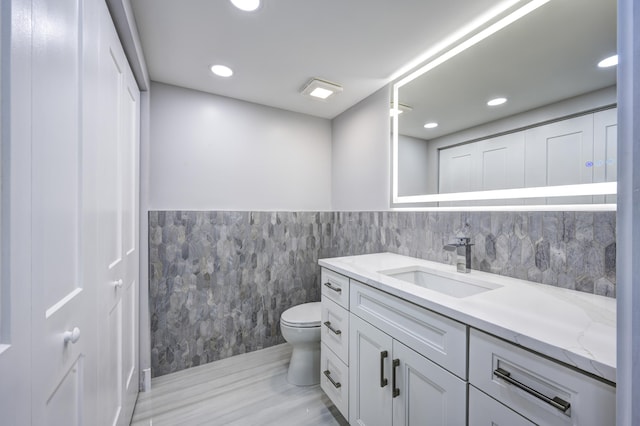 bathroom with hardwood / wood-style flooring, tile walls, toilet, and vanity