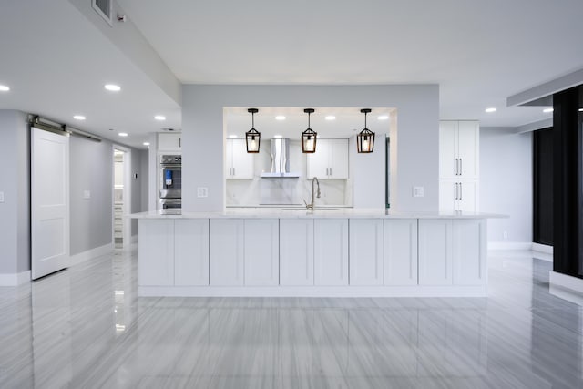 kitchen featuring pendant lighting, wall chimney exhaust hood, white cabinetry, a large island, and a barn door