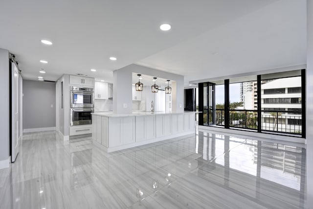 kitchen featuring a barn door, pendant lighting, sink, white cabinetry, and double oven