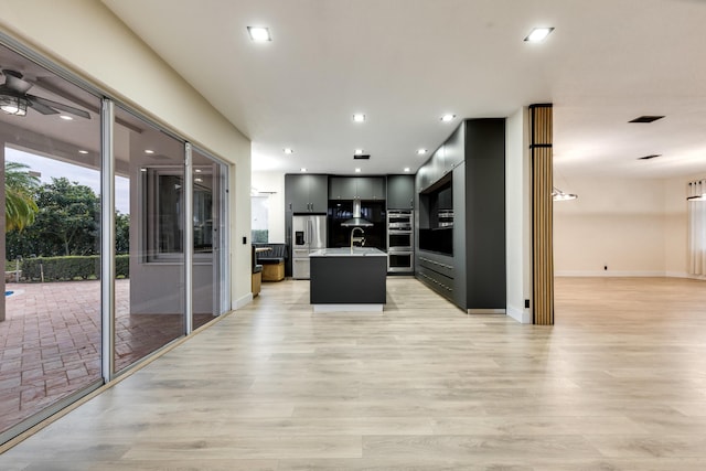 kitchen featuring light hardwood / wood-style floors, ceiling fan, stainless steel appliances, a kitchen island with sink, and sink