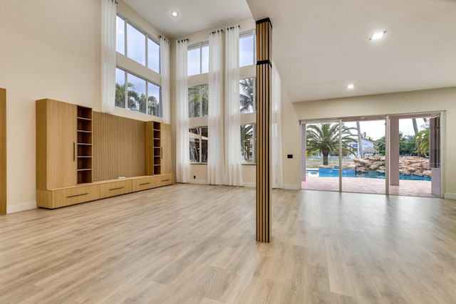 unfurnished living room featuring a towering ceiling and light wood-type flooring