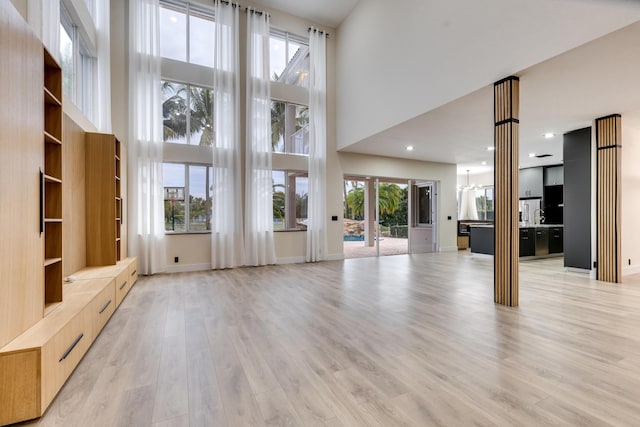 unfurnished living room featuring light hardwood / wood-style flooring, a high ceiling, and a notable chandelier