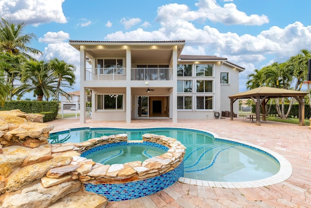 rear view of house with a swimming pool with hot tub, ceiling fan, a patio area, a gazebo, and a balcony