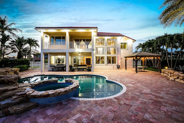 back house at dusk with a pool with hot tub, a gazebo, a balcony, and a patio