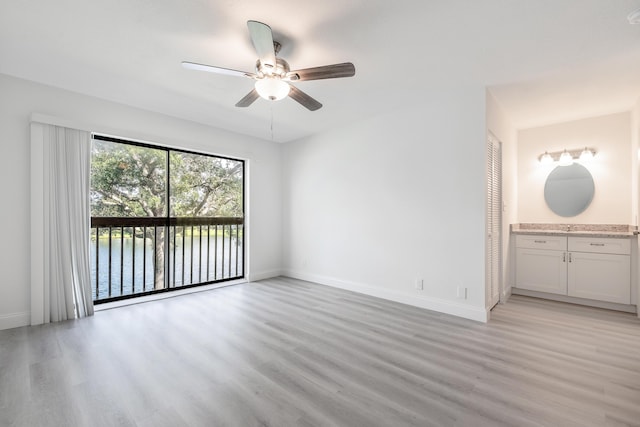 unfurnished bedroom featuring access to outside, a water view, ceiling fan, light hardwood / wood-style floors, and ensuite bath