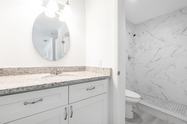 bathroom with tiled shower, vanity, and toilet