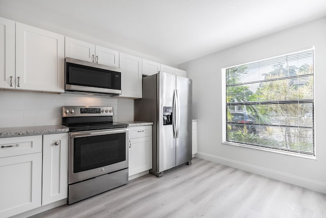 kitchen featuring light stone counters, light hardwood / wood-style floors, decorative backsplash, white cabinets, and appliances with stainless steel finishes