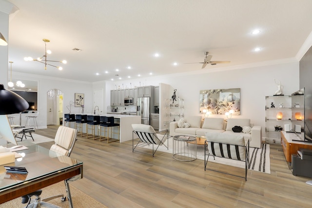 living room featuring light hardwood / wood-style floors, ornamental molding, sink, and ceiling fan with notable chandelier