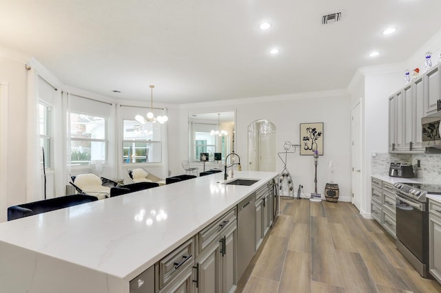 kitchen with a center island with sink, appliances with stainless steel finishes, pendant lighting, sink, and an inviting chandelier