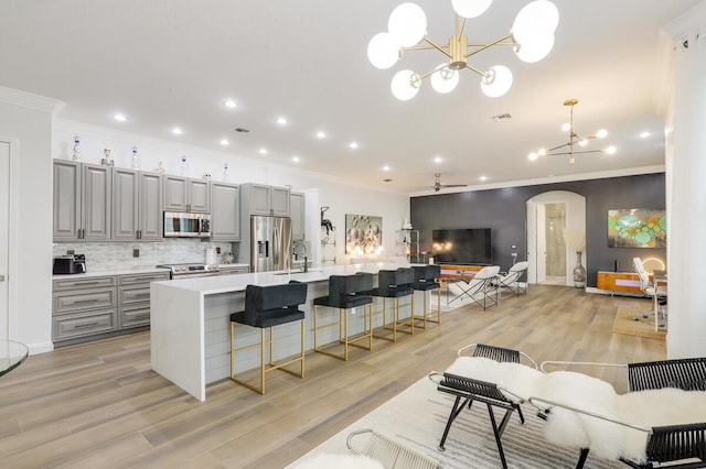 kitchen with decorative light fixtures, stainless steel appliances, a breakfast bar, gray cabinets, and a large island with sink