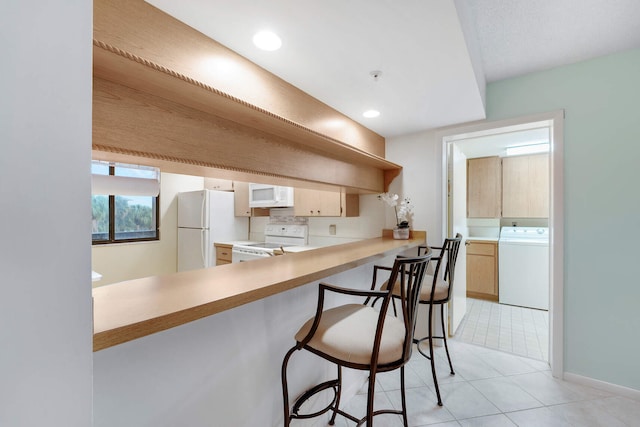 kitchen with light tile patterned floors, white appliances, a breakfast bar area, washer / dryer, and kitchen peninsula