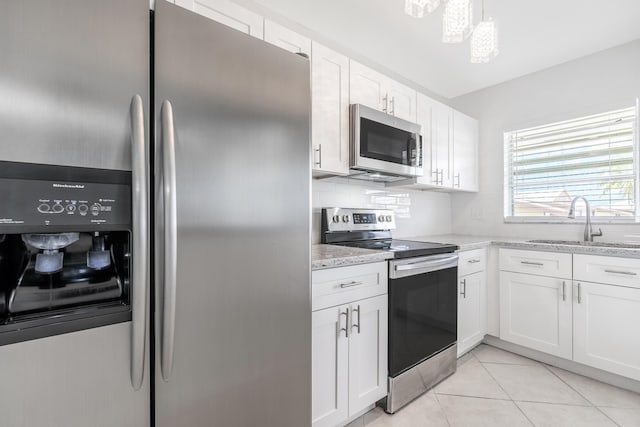 kitchen featuring appliances with stainless steel finishes, white cabinetry, light stone countertops, and sink