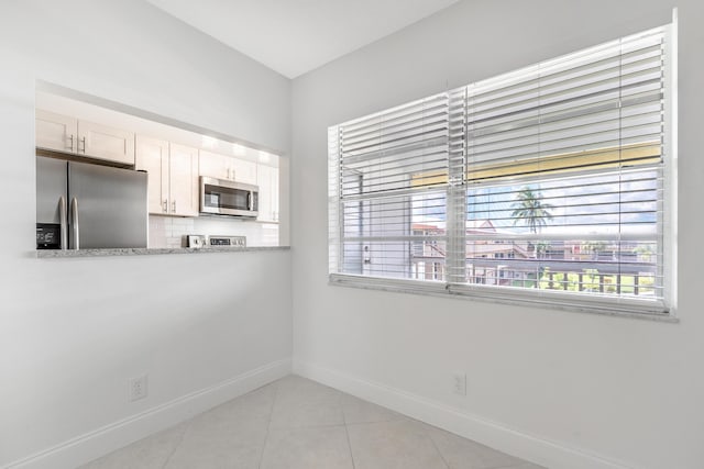 kitchen featuring light stone countertops, light tile patterned floors, tasteful backsplash, white cabinets, and appliances with stainless steel finishes