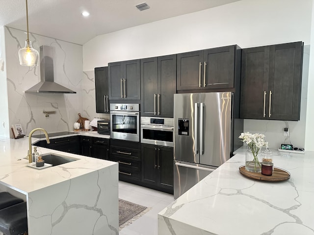 kitchen with stainless steel appliances, light stone counters, decorative backsplash, sink, and wall chimney range hood