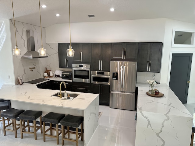 kitchen featuring appliances with stainless steel finishes, kitchen peninsula, a breakfast bar, sink, and wall chimney range hood