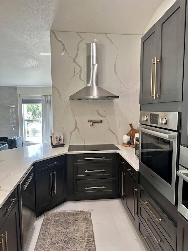 kitchen with a textured ceiling, tasteful backsplash, light stone countertops, wall chimney range hood, and black appliances