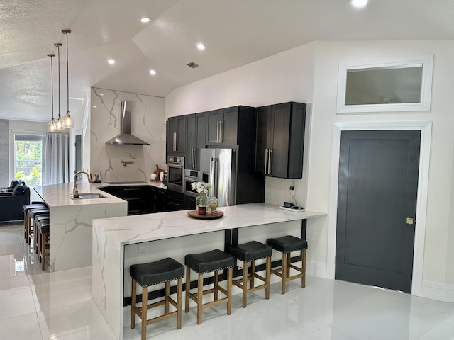 kitchen featuring kitchen peninsula, wall chimney exhaust hood, a breakfast bar, and hanging light fixtures