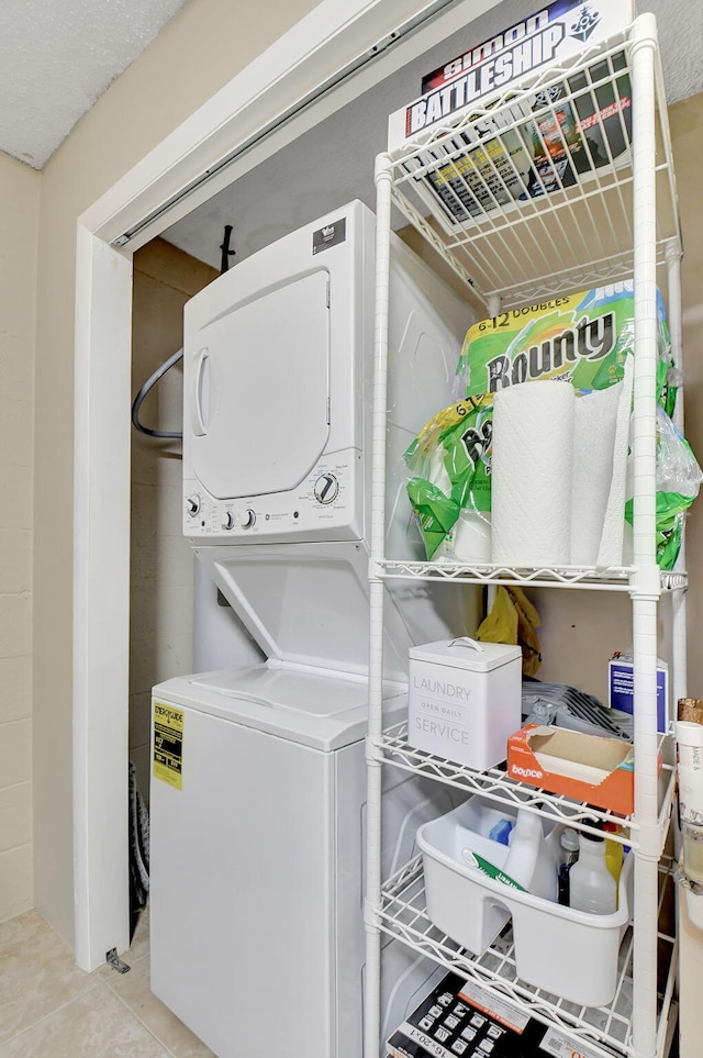 laundry room with stacked washer / dryer, light tile patterned flooring, and a textured ceiling