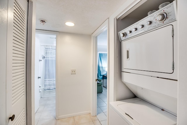 laundry room with light tile patterned floors, a textured ceiling, and stacked washer and dryer