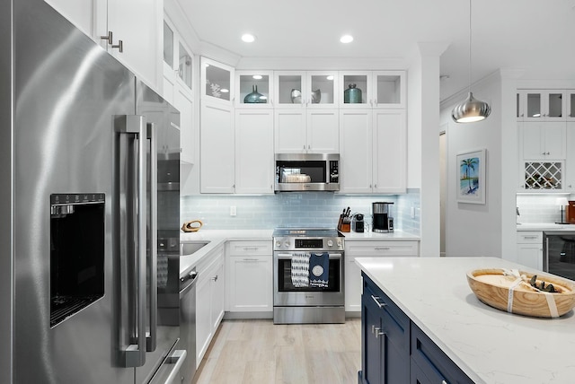 kitchen featuring light stone countertops, decorative light fixtures, tasteful backsplash, white cabinets, and appliances with stainless steel finishes