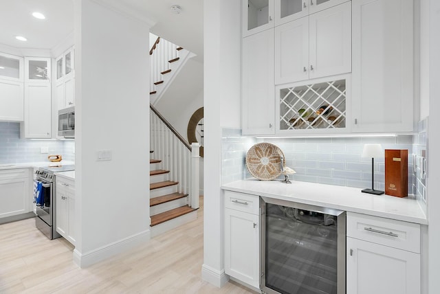 bar with beverage cooler, appliances with stainless steel finishes, light hardwood / wood-style floors, decorative backsplash, and white cabinets