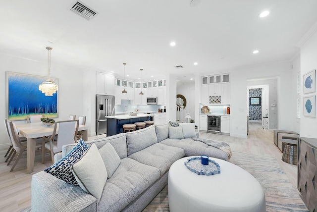 living room with sink, an inviting chandelier, wine cooler, and light hardwood / wood-style flooring