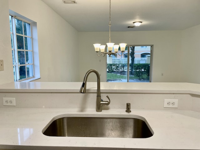 kitchen featuring decorative light fixtures, sink, light stone counters, and an inviting chandelier