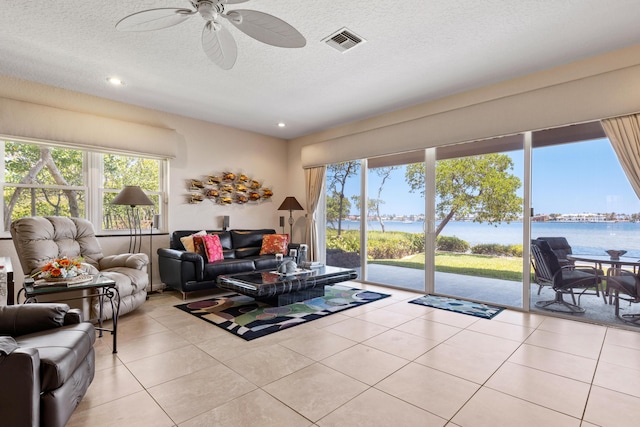 living room with a water view, ceiling fan, light tile patterned flooring, and a textured ceiling