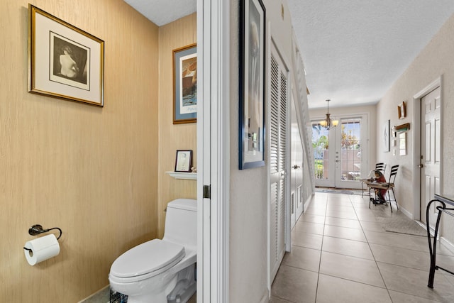 bathroom featuring french doors, tile patterned floors, a textured ceiling, and toilet