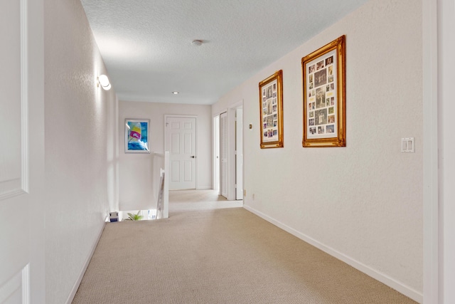 hallway with light colored carpet and a textured ceiling