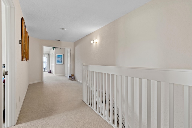 corridor with light carpet and a textured ceiling