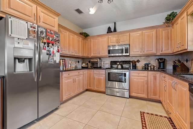 kitchen featuring a textured ceiling, light tile patterned floors, dark stone counters, stainless steel appliances, and decorative backsplash