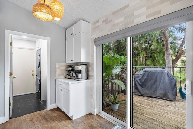 kitchen featuring plenty of natural light, white cabinets, tasteful backsplash, and stacked washer / dryer