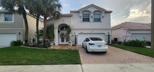 mediterranean / spanish-style home featuring stucco siding, decorative driveway, an attached garage, and a front lawn