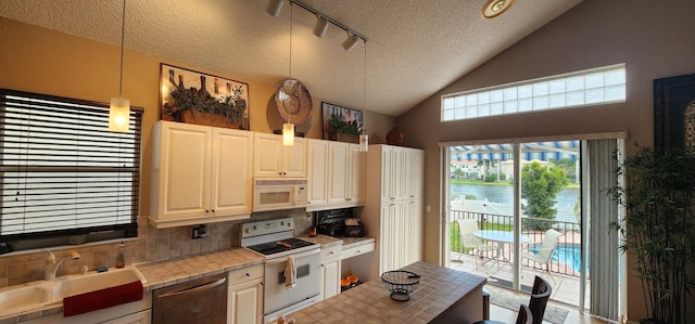 kitchen with a sink, a water view, rail lighting, white appliances, and backsplash