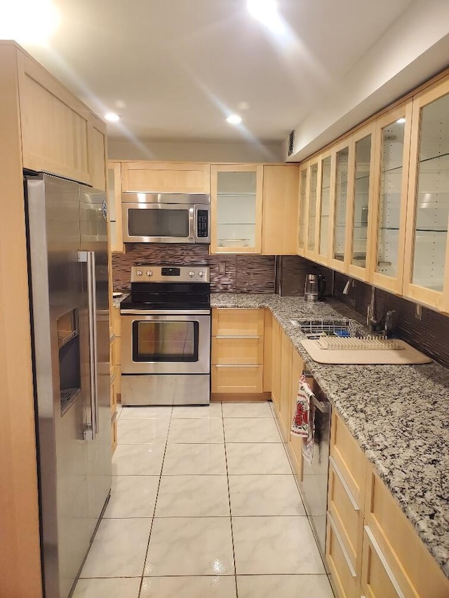 kitchen with light stone countertops, stainless steel appliances, light tile patterned floors, tasteful backsplash, and light brown cabinets