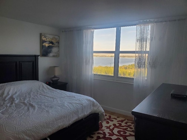 bedroom with hardwood / wood-style flooring and a water view