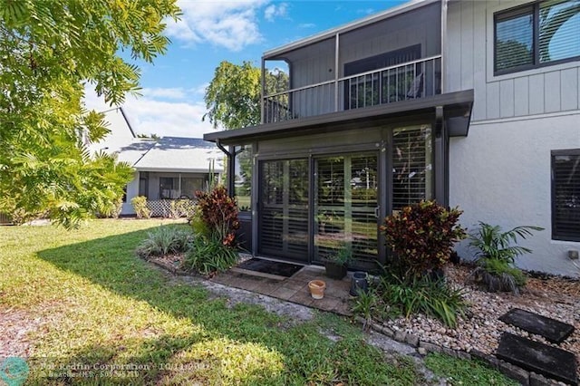 back of house with a balcony, stucco siding, and a yard