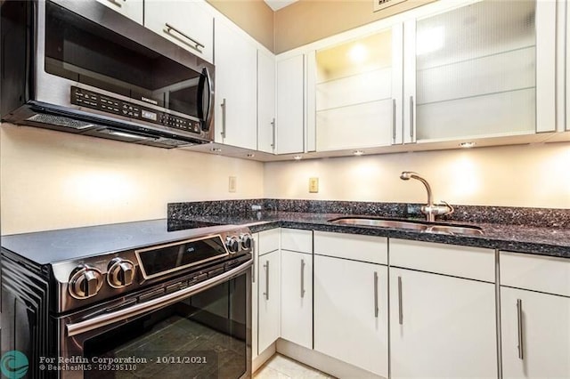 kitchen featuring dark stone counters, stainless steel appliances, a sink, and white cabinets