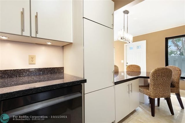 kitchen featuring decorative light fixtures, light tile patterned floors, white cabinetry, dark stone countertops, and dishwashing machine