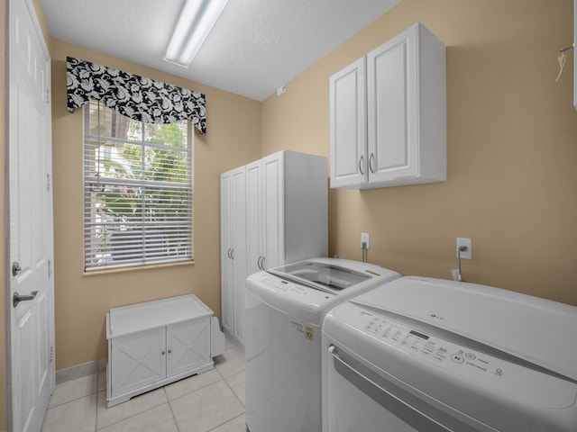 clothes washing area with cabinets, washing machine and clothes dryer, a textured ceiling, and light tile patterned floors