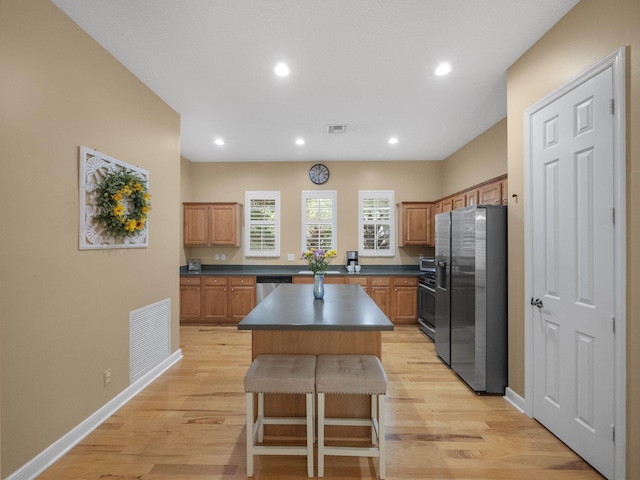 kitchen featuring light wood-type flooring, a kitchen island, a kitchen breakfast bar, and appliances with stainless steel finishes