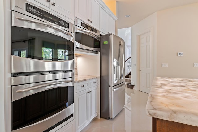 kitchen with stainless steel appliances, white cabinets, light tile patterned floors, and light stone counters