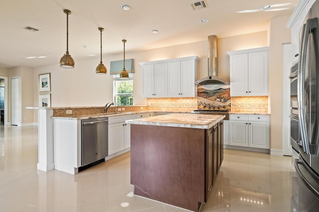 kitchen featuring wall chimney exhaust hood, a center island, decorative light fixtures, stainless steel appliances, and white cabinets