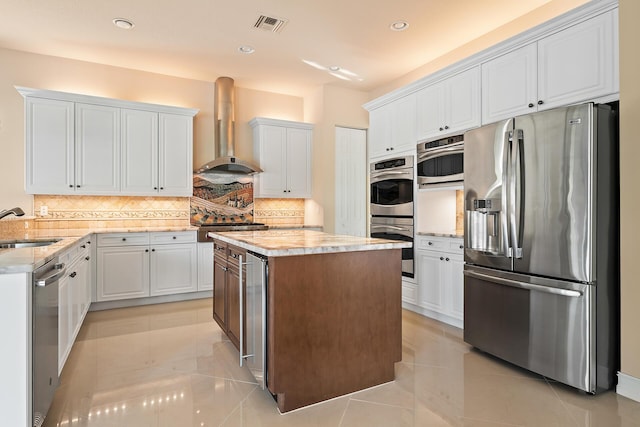 kitchen featuring a center island, wall chimney range hood, light tile patterned floors, white cabinetry, and appliances with stainless steel finishes