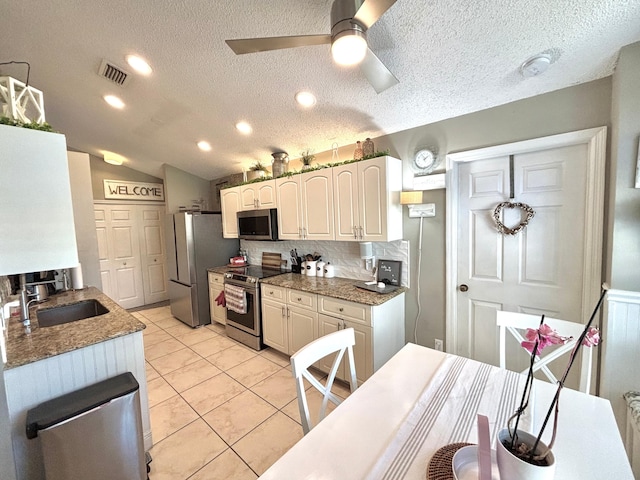 kitchen with appliances with stainless steel finishes, tasteful backsplash, lofted ceiling, white cabinets, and light tile patterned floors