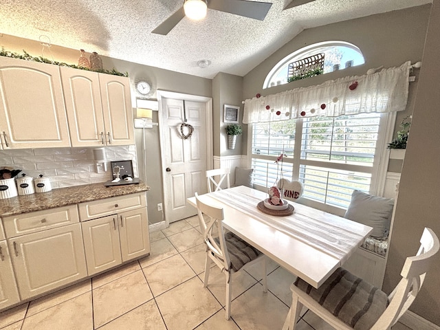 dining space featuring light tile patterned flooring, ceiling fan, vaulted ceiling, and a textured ceiling